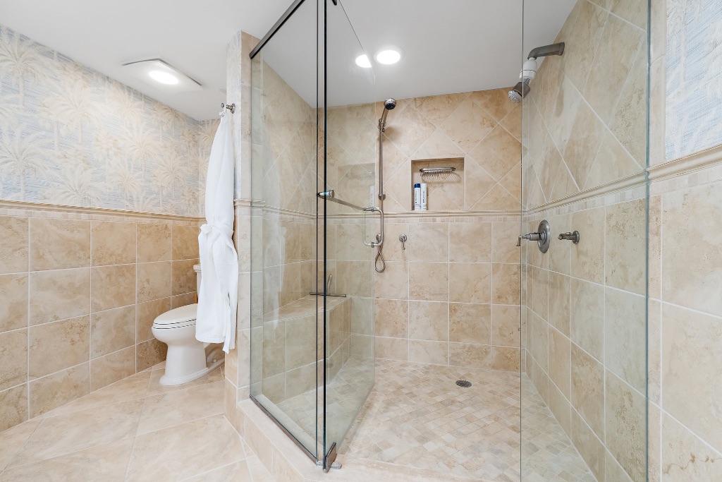 Primary bathroom walk-in shower with travertine tile and multiple shower heads