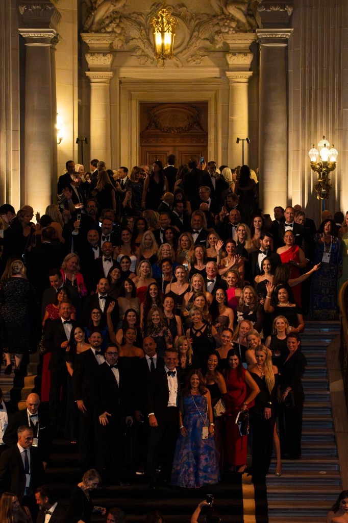 A crowd of Sotheby's International Realty advisors in formal evening wear pose on the illuminated grand staircase during the 50th anniversary gala in San Francisco