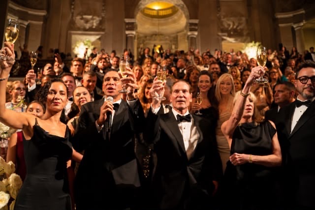 Speakers and guests raise champagne glasses in a celebratory toast during the Sotheby's International Realty 50th anniversary gala in a grand classical ballroom